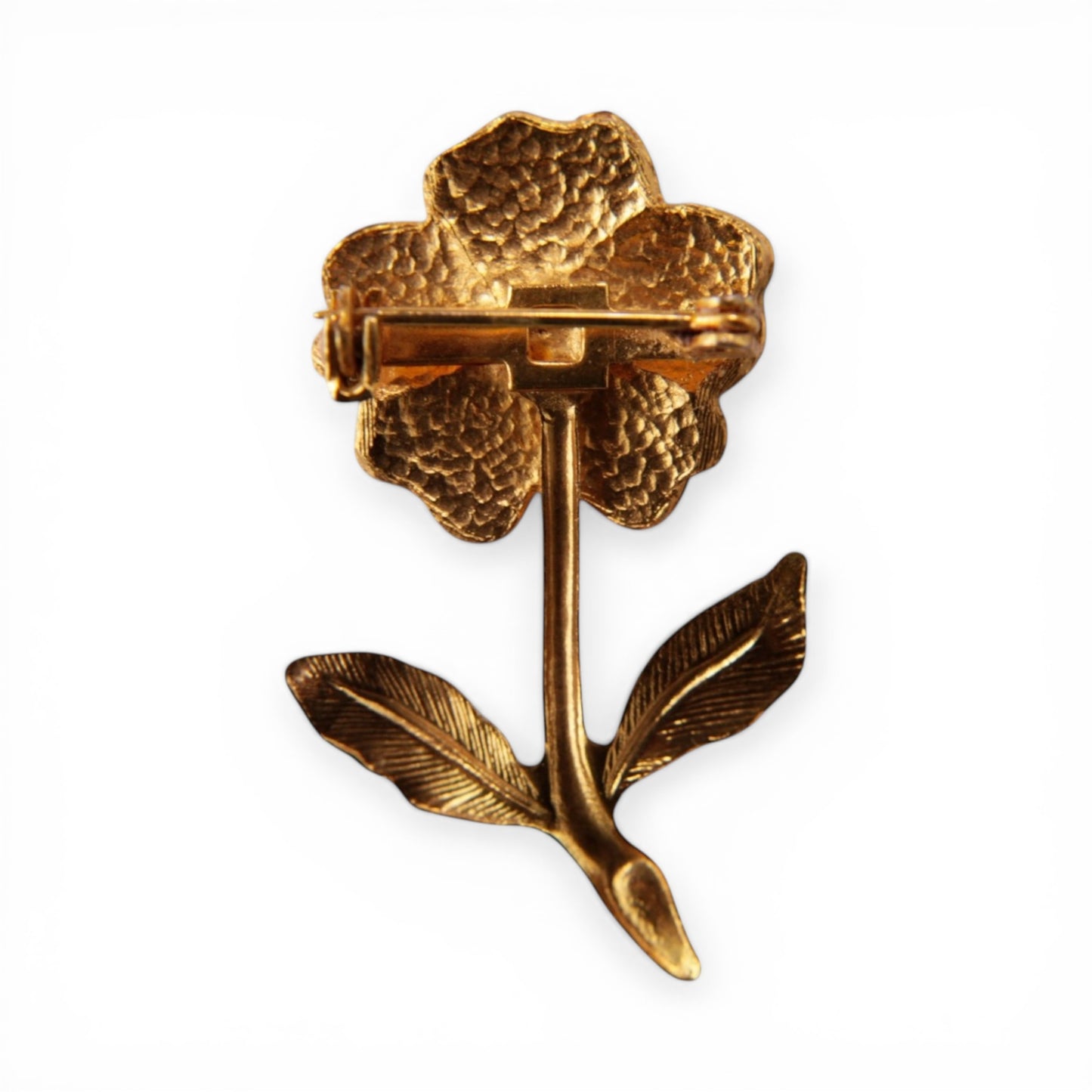 Reverse of gold-tone flower brooch showing pebbled cast texture and horizontal roll-over bar pin clasp with C-catch mounte...