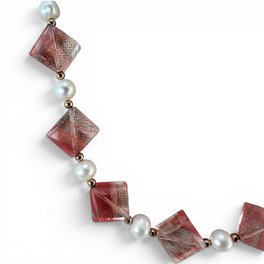 Close-up of faceted translucent coral-red square-cut glass beads drilled point-to-point on gold-tone wire with pearl and s...