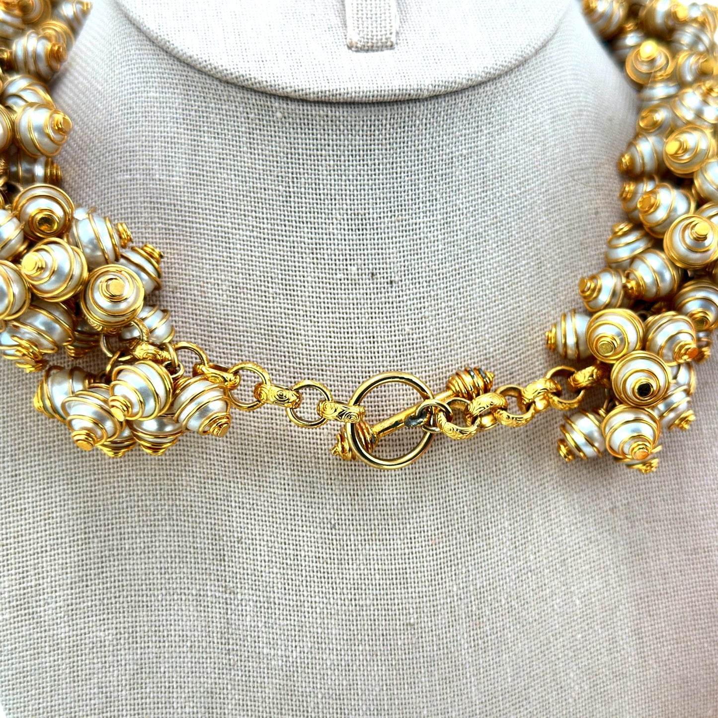 Close-up of spiral gold-tone wire-caged faux pearl beads and ornate ring-and-bar toggle clasp on bib necklace, back view