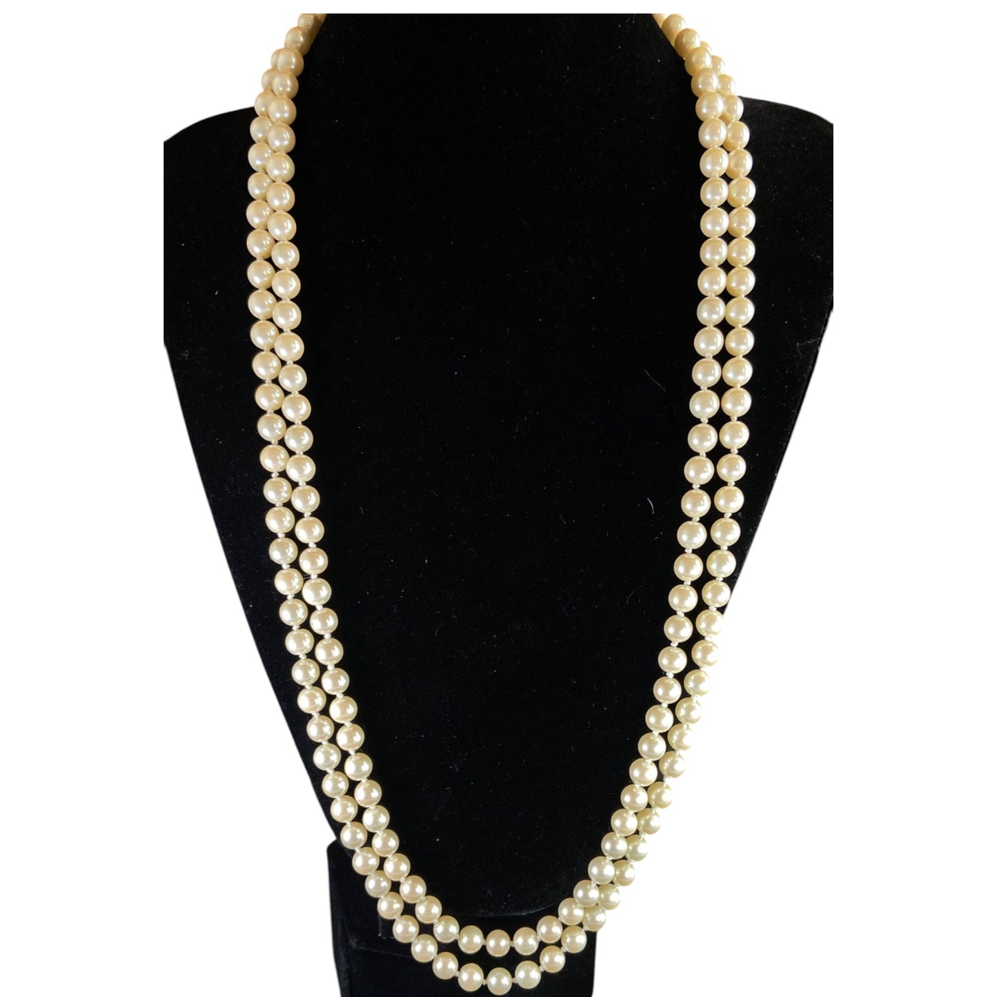 Long single-strand cream faux pearl necklace by Monet displayed doubled on a black bust form, showing full length