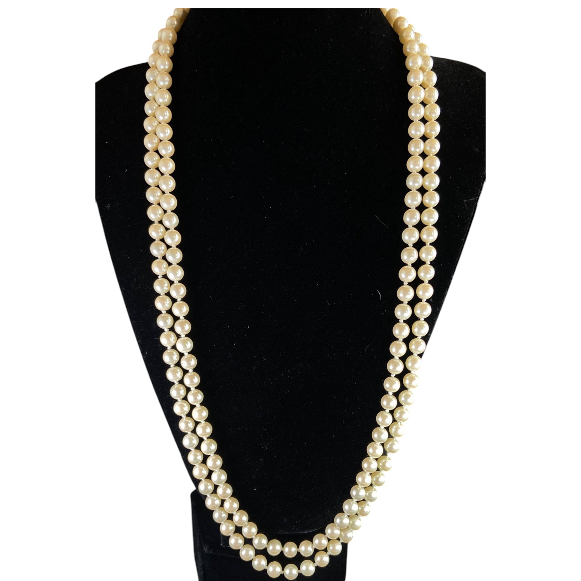 Long single-strand cream faux pearl necklace by Monet displayed doubled on a black bust form, showing full length