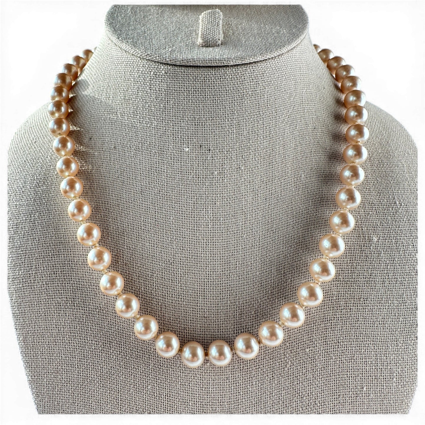 Single-strand champagne faux pearl necklace with hand-knotted cord, laid flat on neutral surface, full length view