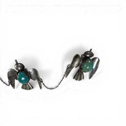 Close-up of stylized flat sheet metal bird figure with ball head and teal turquoise cabochon at chest, oxidized silver patina