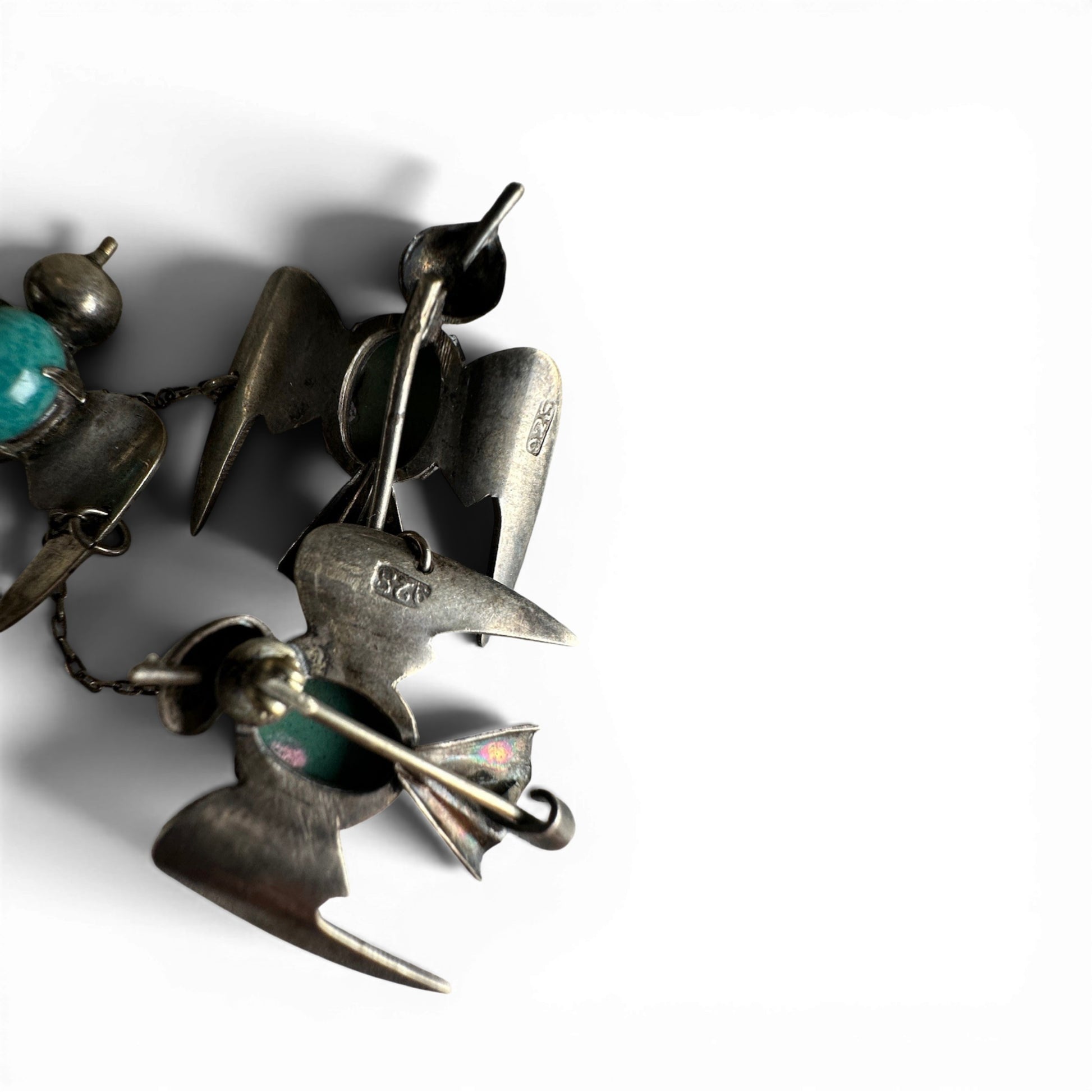 Reverse of three bird brooches showing C-catch pin stems and 925 hallmark stamps on metal