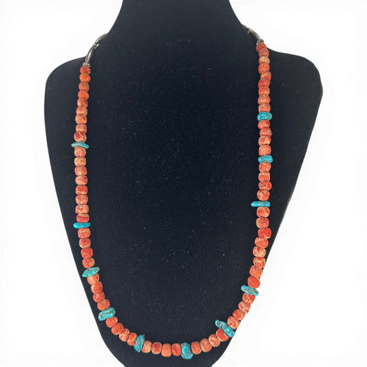Single-strand necklace with orange-red coral rondelles and irregular turquoise chip beads on a white surface
