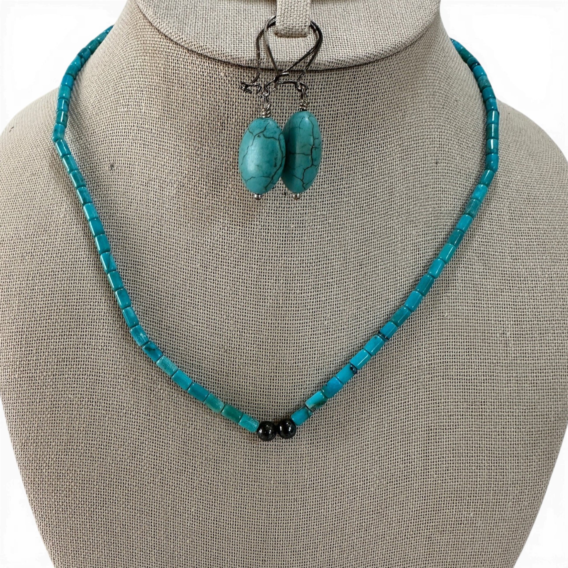 Teal tube-bead necklace with two round black hematite center accents displayed on a linen bust form, 17.5 inches long