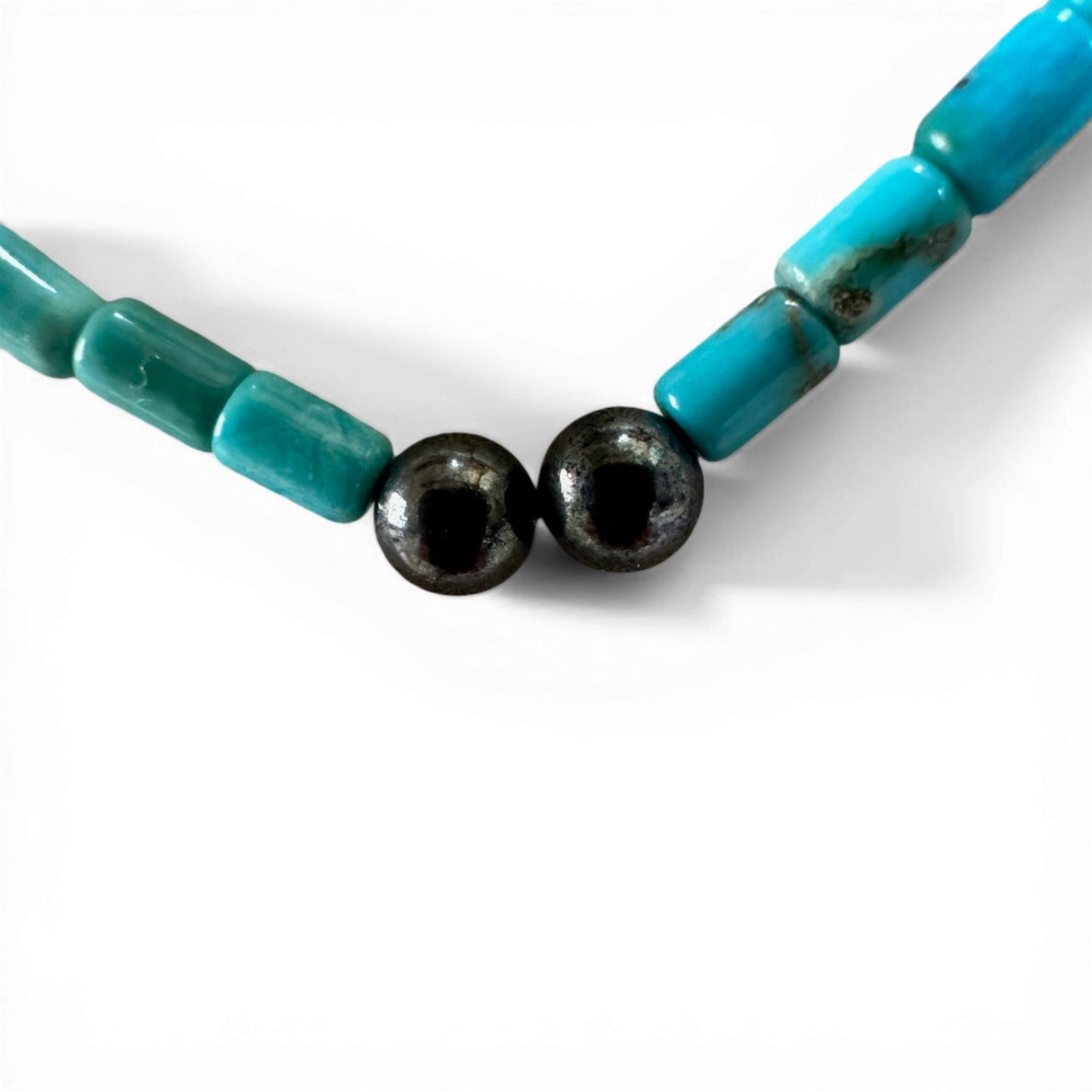 Close-up of two round black hematite accent beads at the center front of a teal tube-bead necklace strand