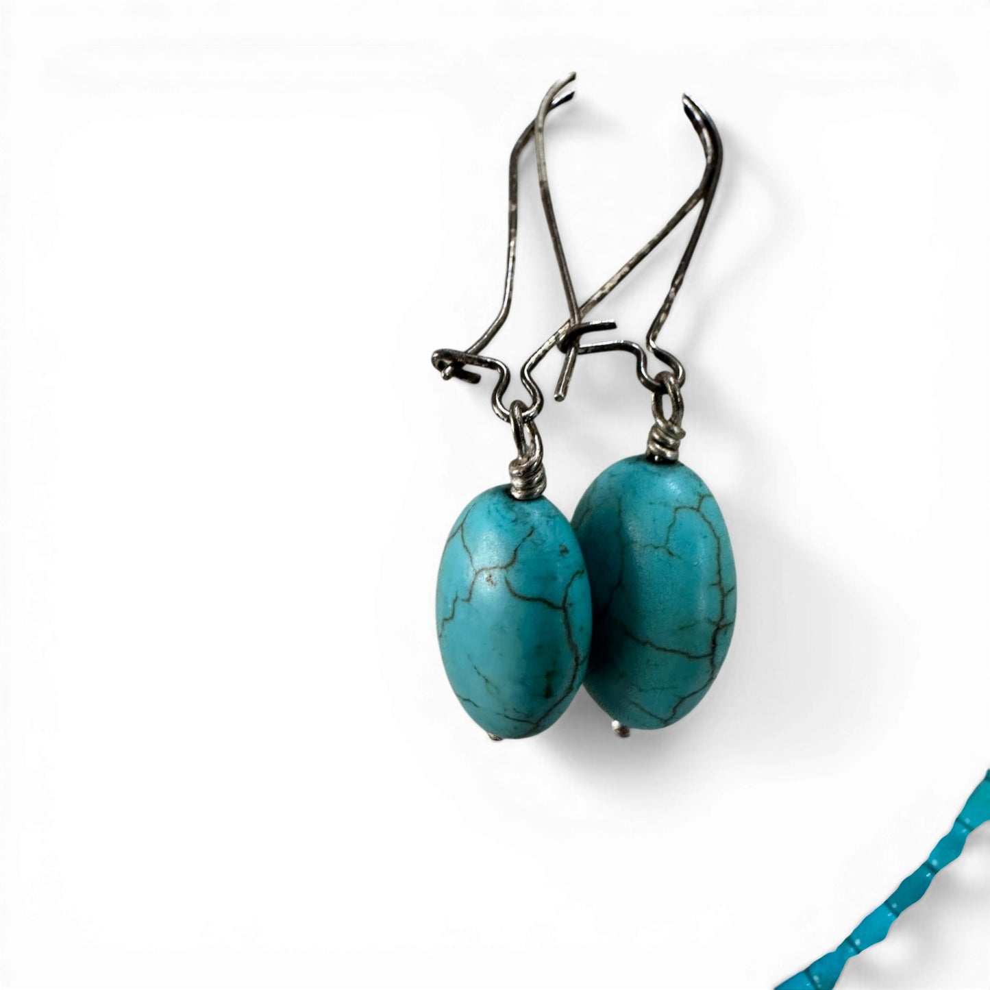 Detail of oval faux turquoise earring drop with coiled wire wrap and small silver-tone bead cap at base