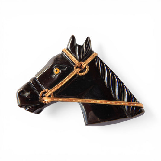 Carved black jet horse head brooch in left-facing profile with gold-toned bridle and amber tiger's eye eye inset, approx. ...