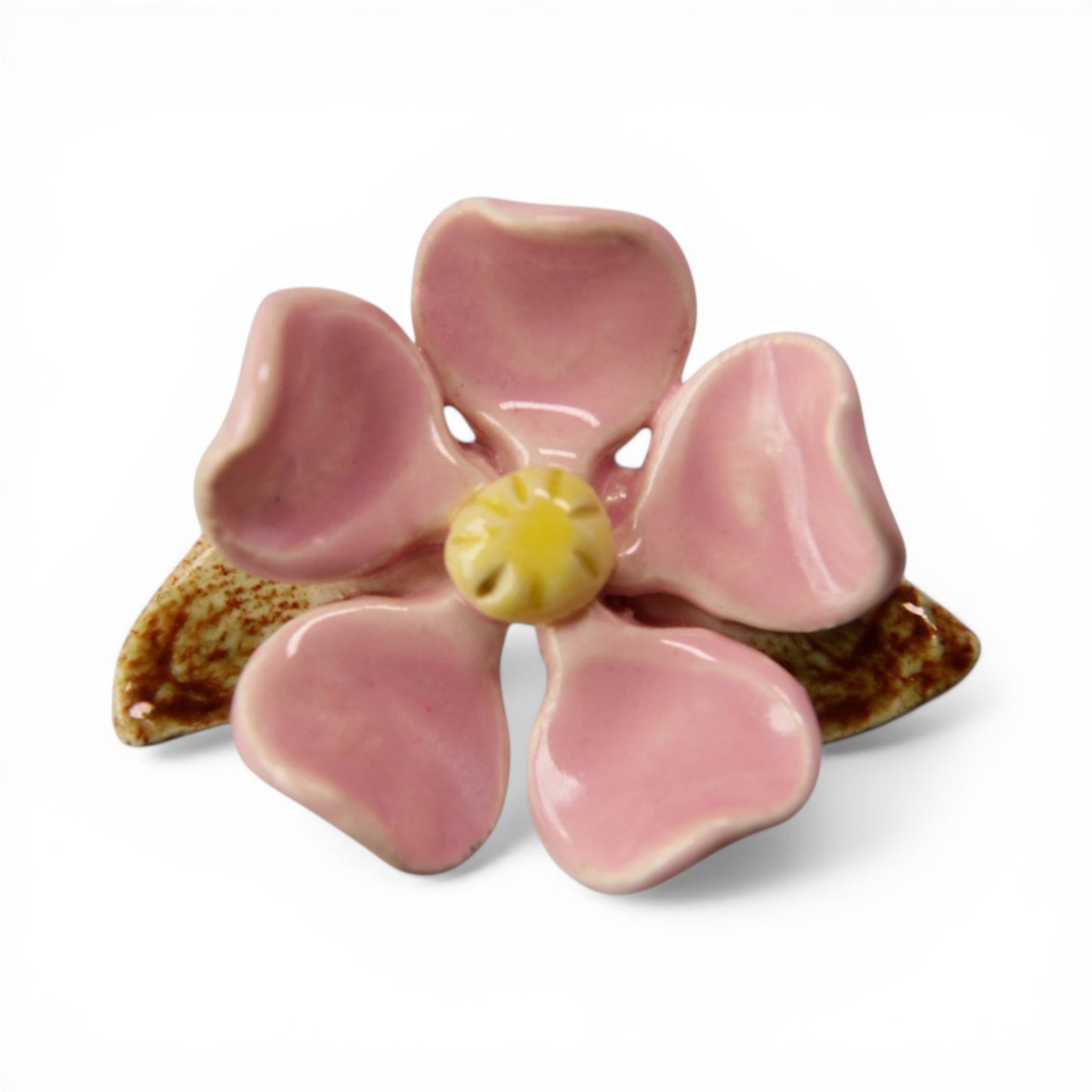 Hand-formed ceramic flower brooch with five dusty rose petals, pale yellow stamen, and brown glazed leaves, front view