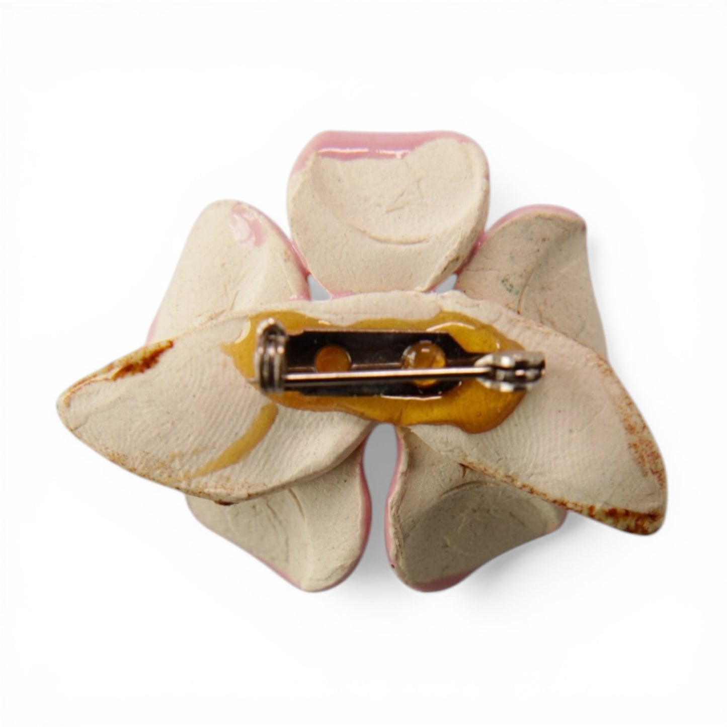 Reverse of ceramic flower brooch showing unglazed off-white raw clay body and standard roll-over C-catch pin-back hardware...