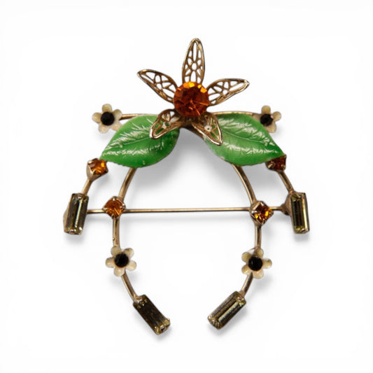 Gold-tone horseshoe brooch with cream enamel daisy flowers, amber rhinestones, and olive baguettes arranged around the arc...