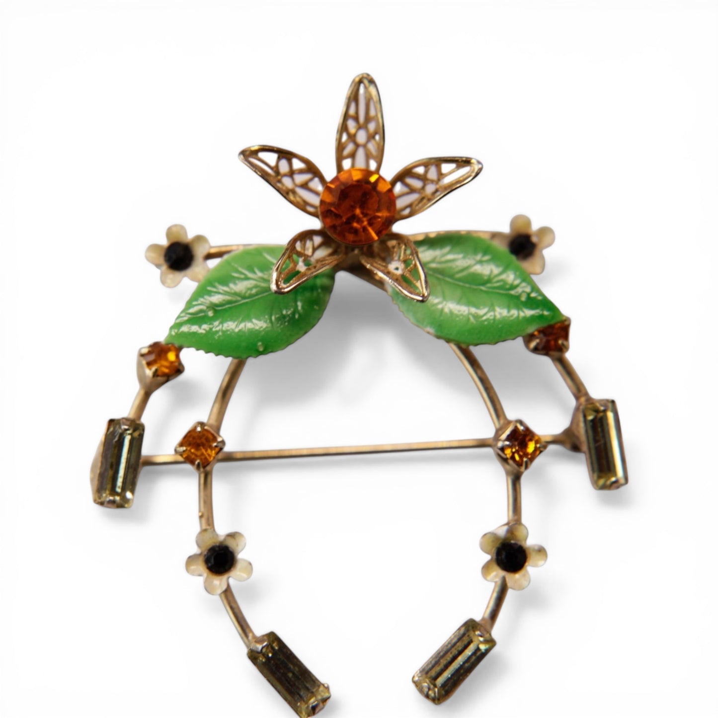 Gold-tone horseshoe brooch with central filigree flower, amber round rhinestone center, and two green enamel leaves at the...