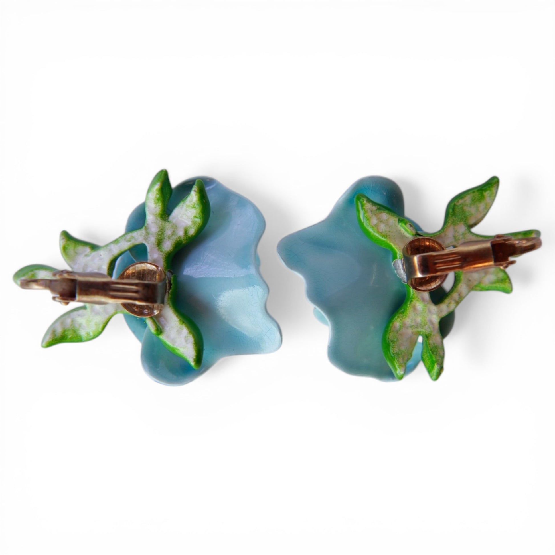 Reverse of powder blue Lucite floral clip-on earrings showing copper-tone paddle clip mechanism and green enamel leaf base
