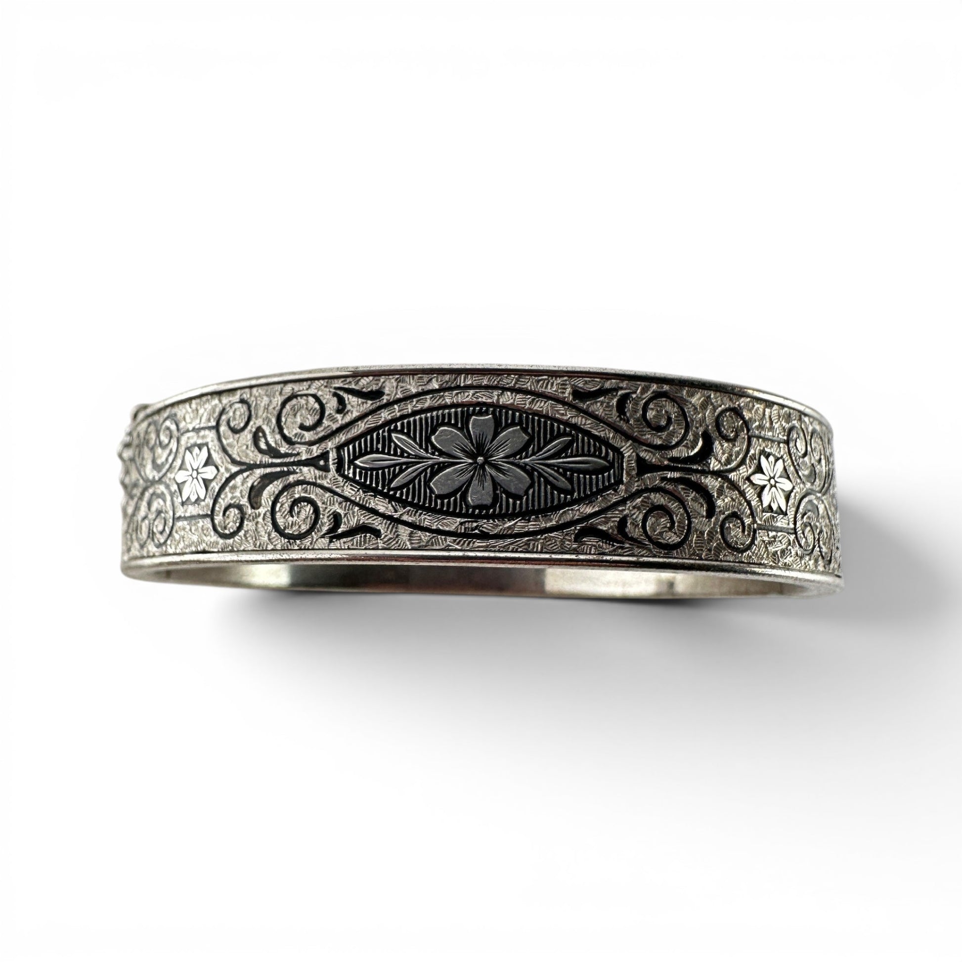 Wide sterling silver hinged bangle bracelet with niello-filled engraved floral and scrollwork decoration across outer surf...