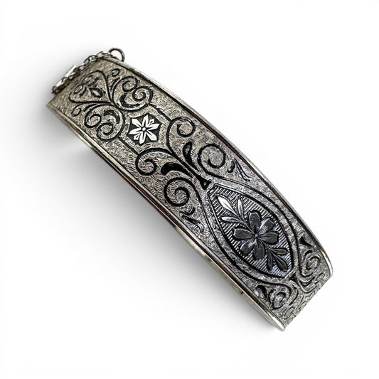 Close-up of central oval cartouche on sterling silver bangle showing engraved flower motif flanked by leaf sprays and scro...