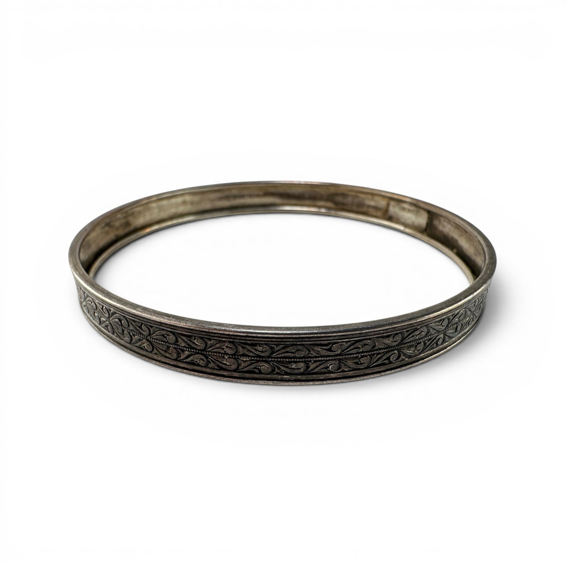 Hinged sterling silver bangle by Coro with continuous scrolling foliate engraving on flat outer face, oxidized finish