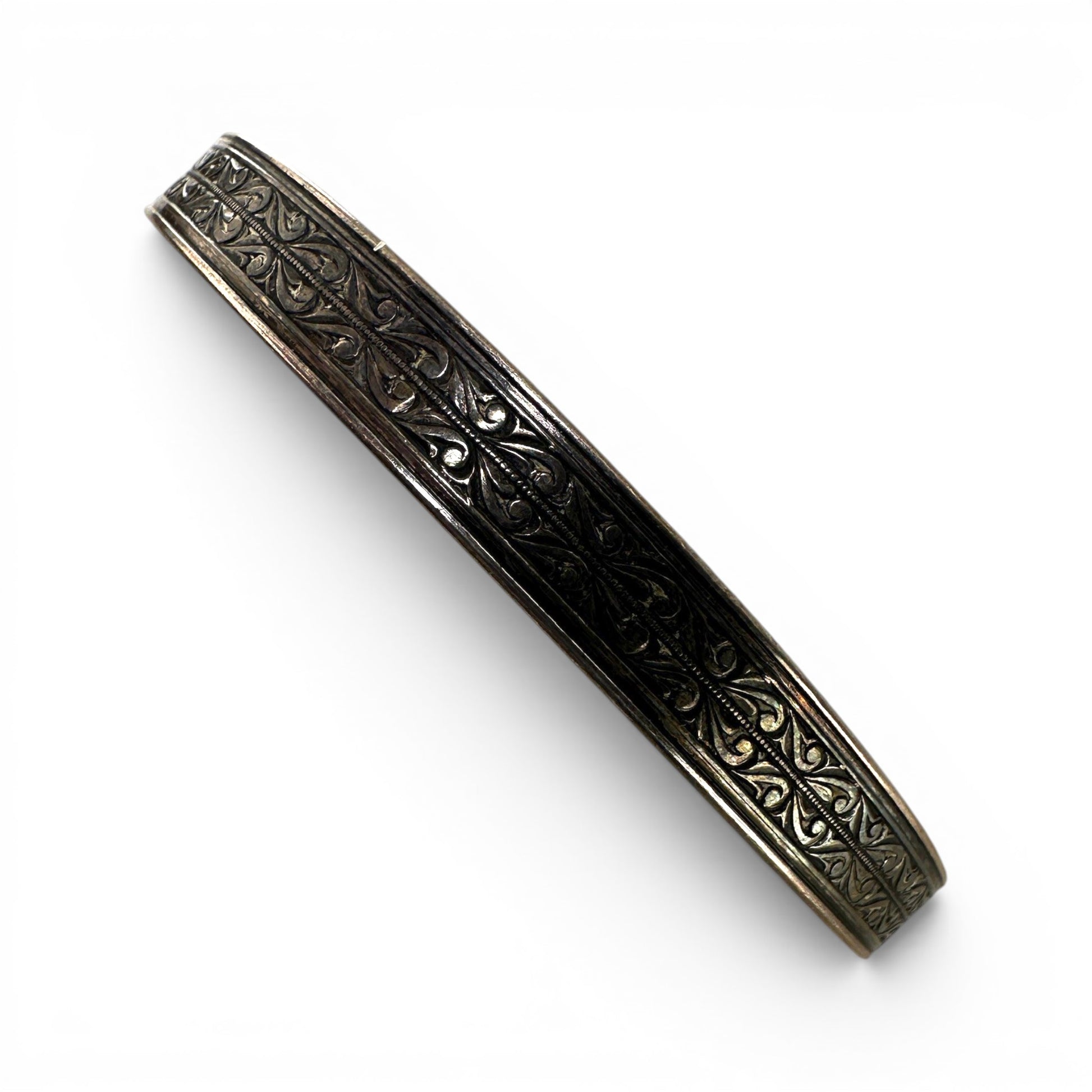 Close-up of engraved arabesque and foliate motifs on oxidized sterling silver bangle with raised parallel border edges