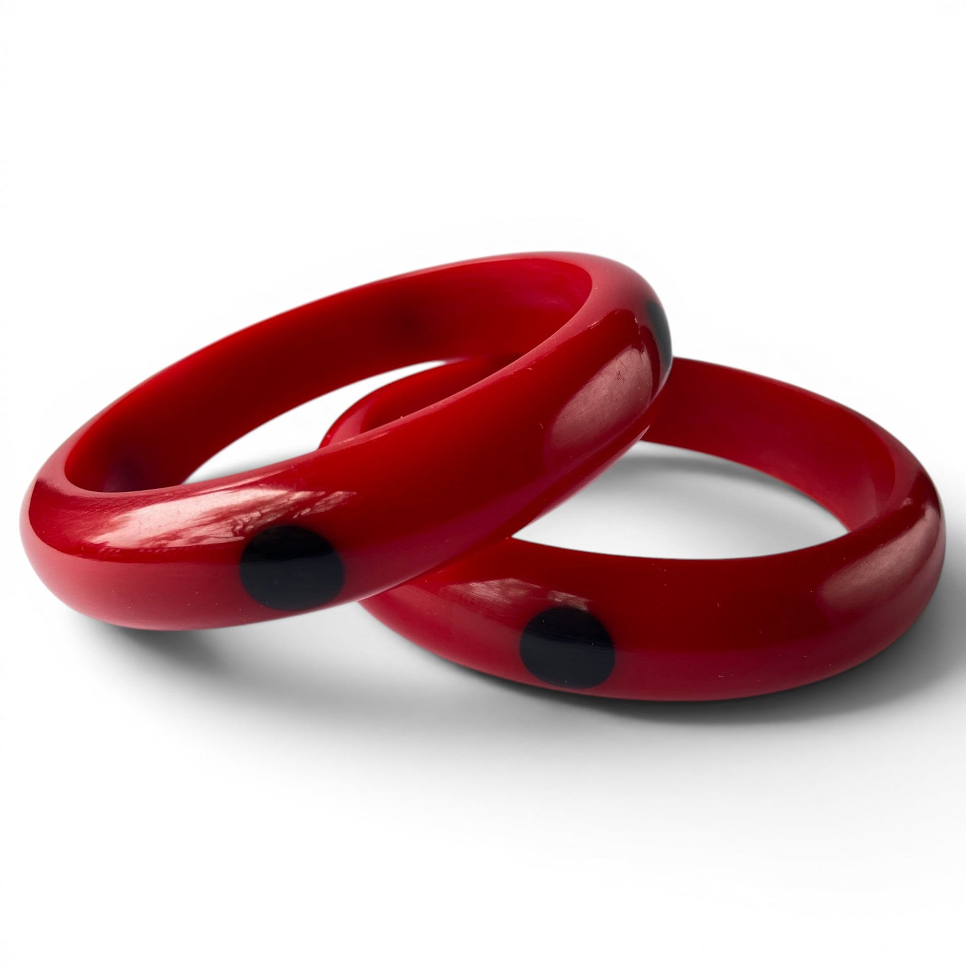 Pair of chunky cherry red Bakelite slip-on bangles, one with evenly spaced flush-inlaid navy black oval dots, one plain, d...