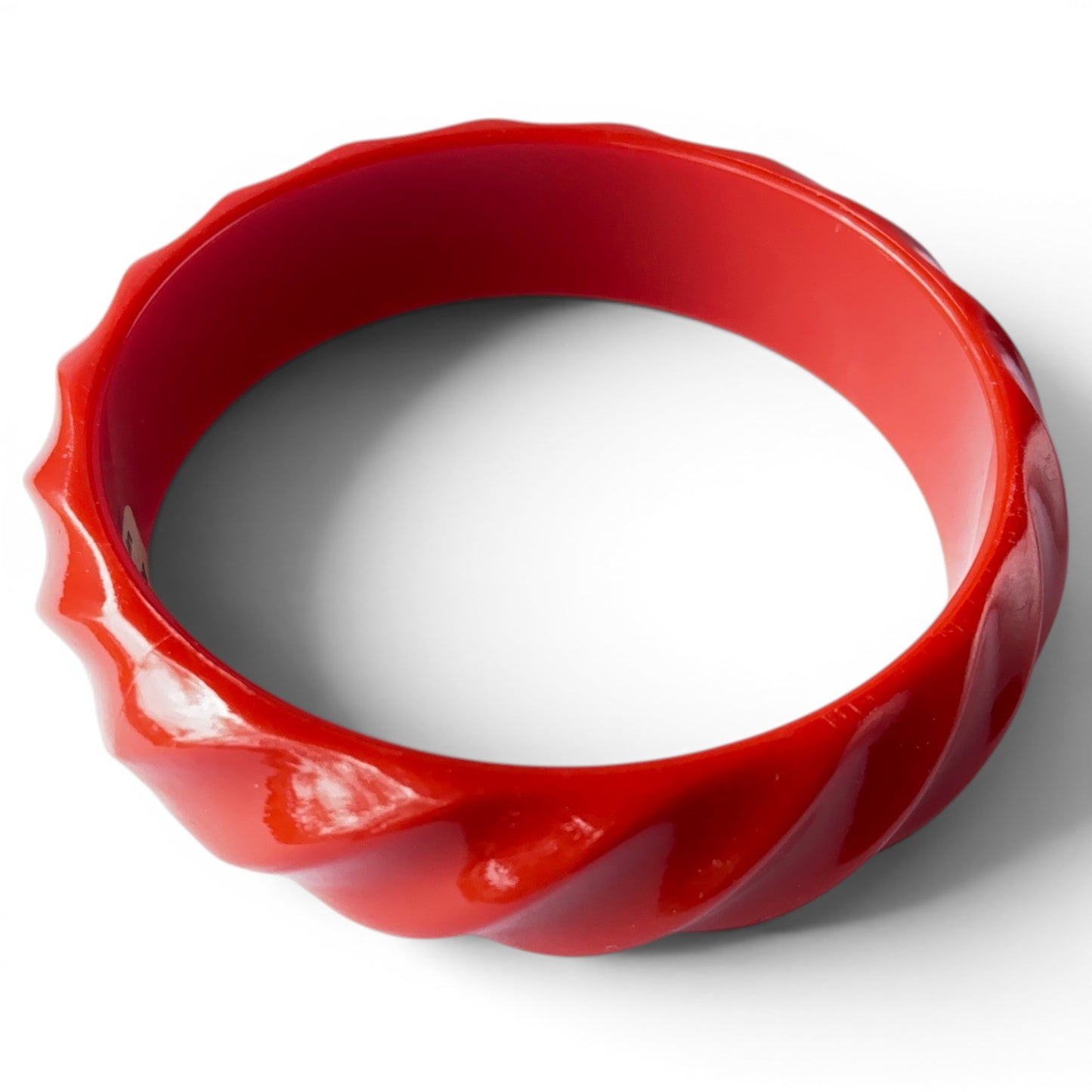 Top-down view of cherry red Bakelite bangle showing ridged outer edge, smooth interior bore, and small tan paper label rea...