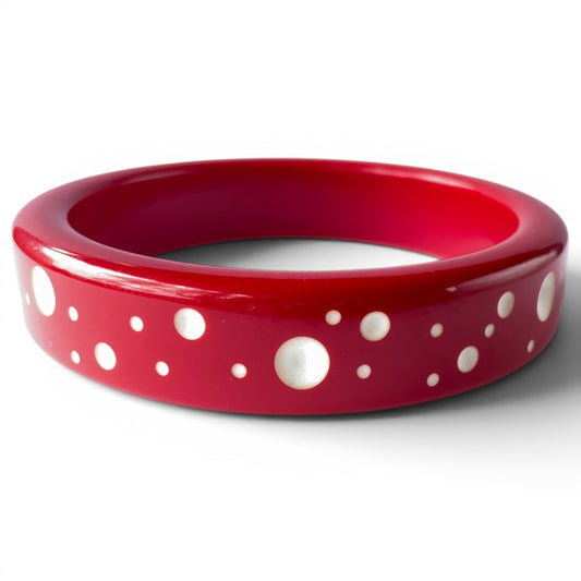 Wide cherry red Bakelite bangle with scattered white dot of varying sizes along outer band