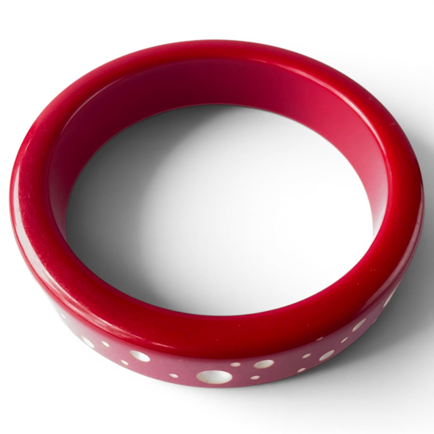 Close-up of cherry red Bakelite bangle showing flush-inlaid white and cream mother of pearl dots ranging from pinpoint to ...