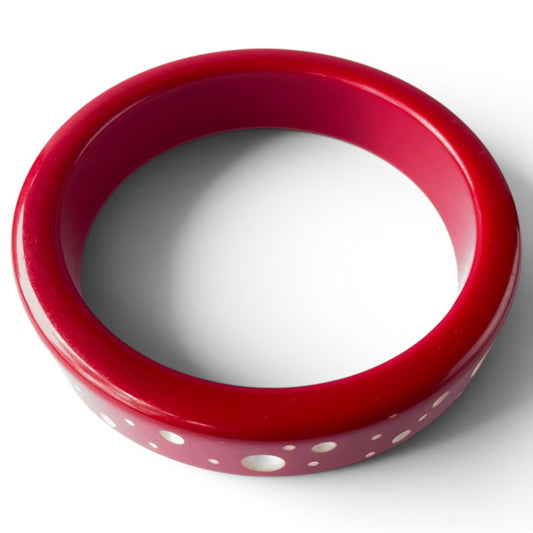 Close-up of cherry red Bakelite bangle showing flush-inlaid white and cream mother of pearl dots ranging from pinpoint to ...
