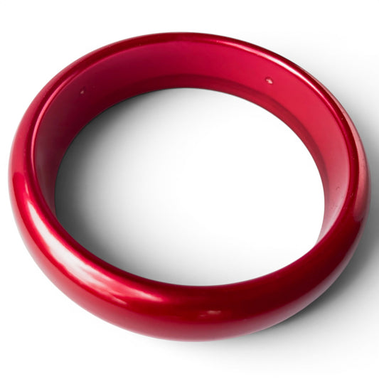 Close-up of seamless one-piece red Bakelite bangle showing rounded convex profile and smooth interior bore, minor age pits...