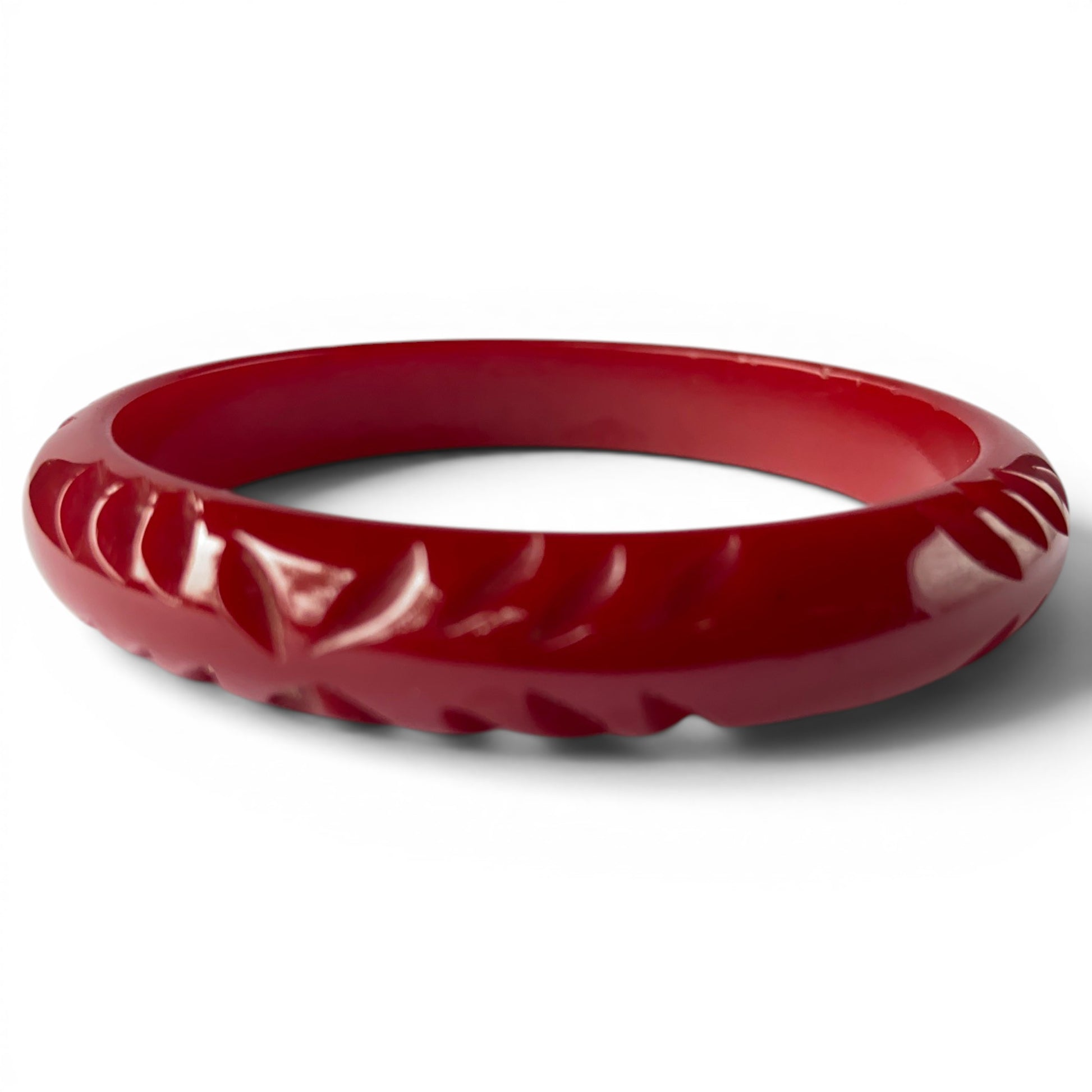 Deep cherry red carved Bakelite bangle with domed profile and incised leaf and petal motifs around the circumference