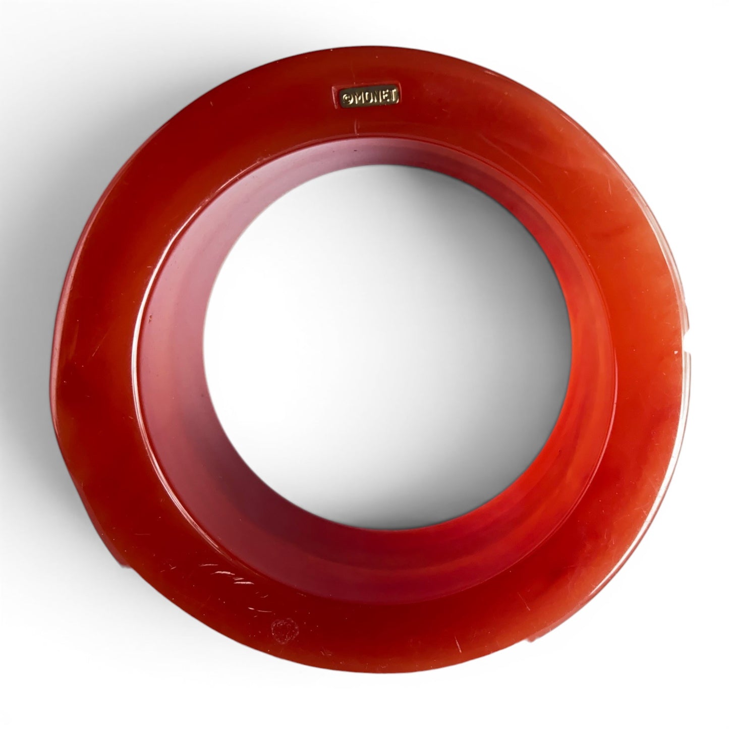 Side view of red-orange Lucite bangle showing concave waist, flared top and bottom rims, smooth circular interior bore