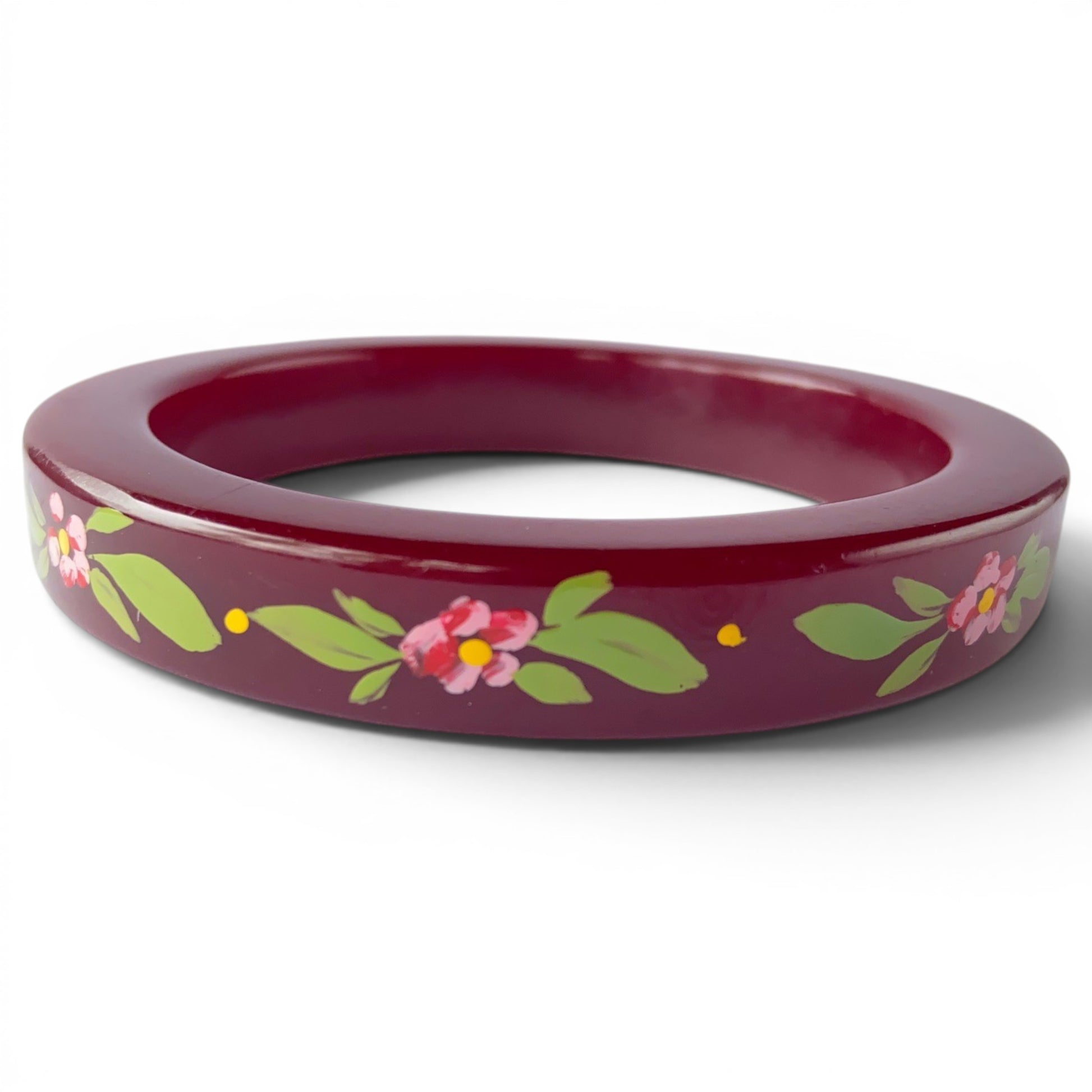 Wide burgundy Lucite bangle with hand-painted pink floral motif, yellow centers, and green leaves on flat outer face