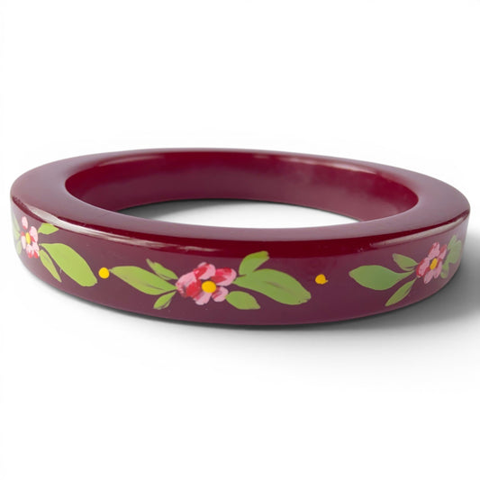 Wide burgundy Lucite bangle with hand-painted pink floral motif, yellow centers, and green leaves on flat outer face
