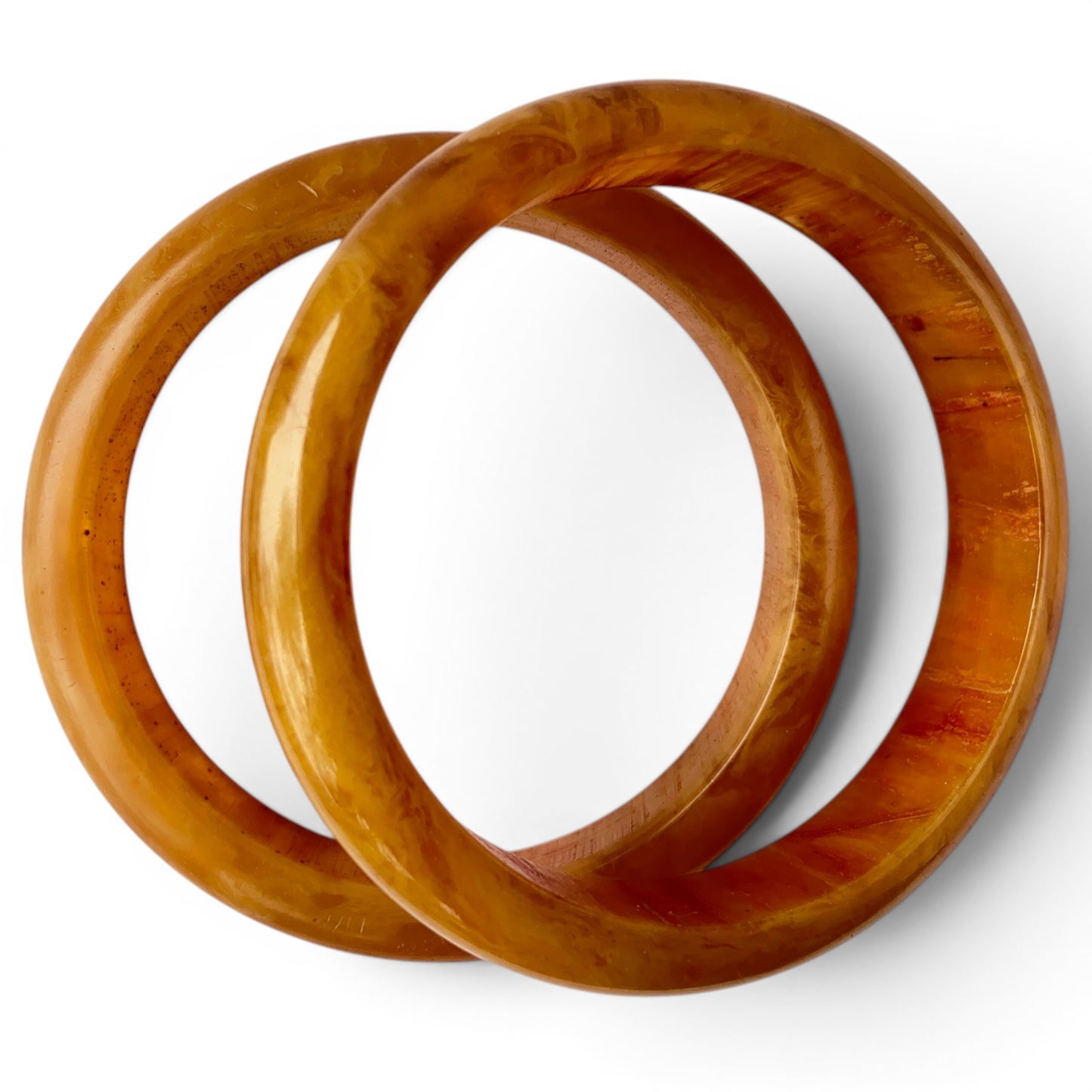 Two chunky tubular Bakelite bangles showing warm honey-amber base color with deep caramel and reddish-brown streaks throug...
