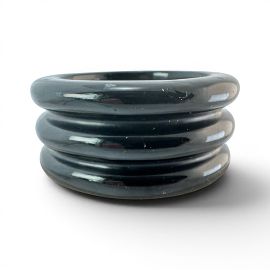 Close view of triple concentric raised ridges on black Bakelite bangle showing dark green-gray undertones in surface color...