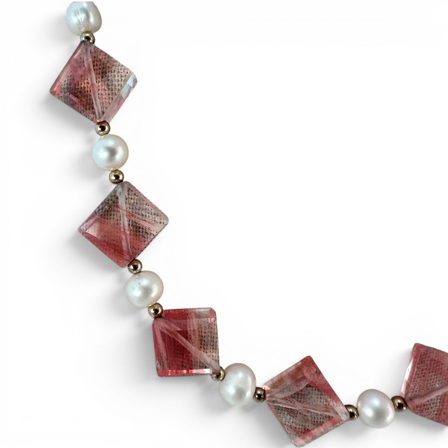 Close-up of faceted translucent coral-red square-cut glass beads drilled point-to-point on gold-tone wire with pearl and s...