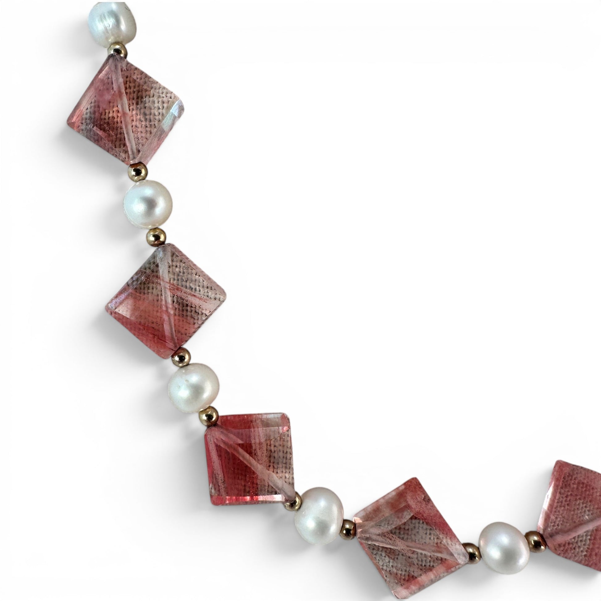 Close-up of faceted translucent coral-red square-cut glass beads drilled point-to-point on gold-tone wire with pearl and s...