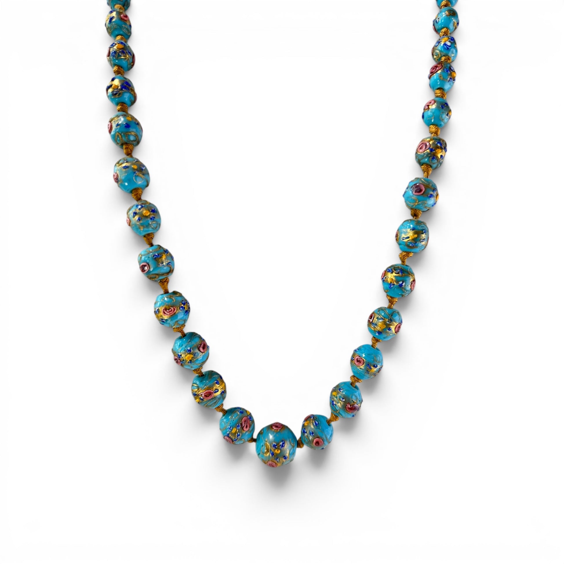 Close-up of hand-painted Murano glass beads showing raised pink, cobalt blue, and gold floral decoration on turquoise-blue...