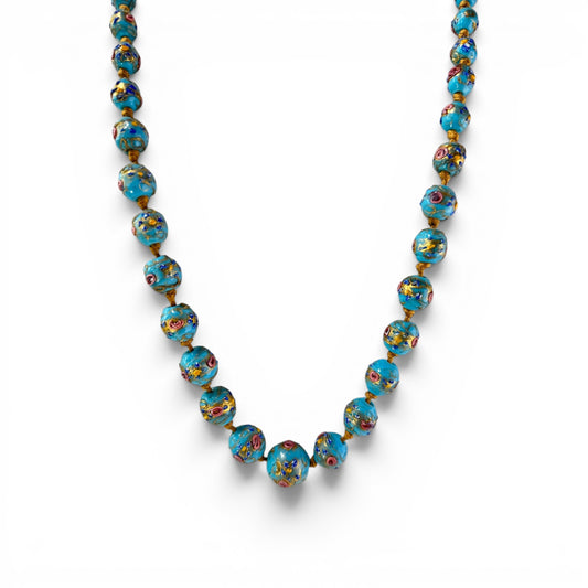 Close-up of hand-painted Murano glass beads showing raised pink, cobalt blue, and gold floral decoration on turquoise-blue...