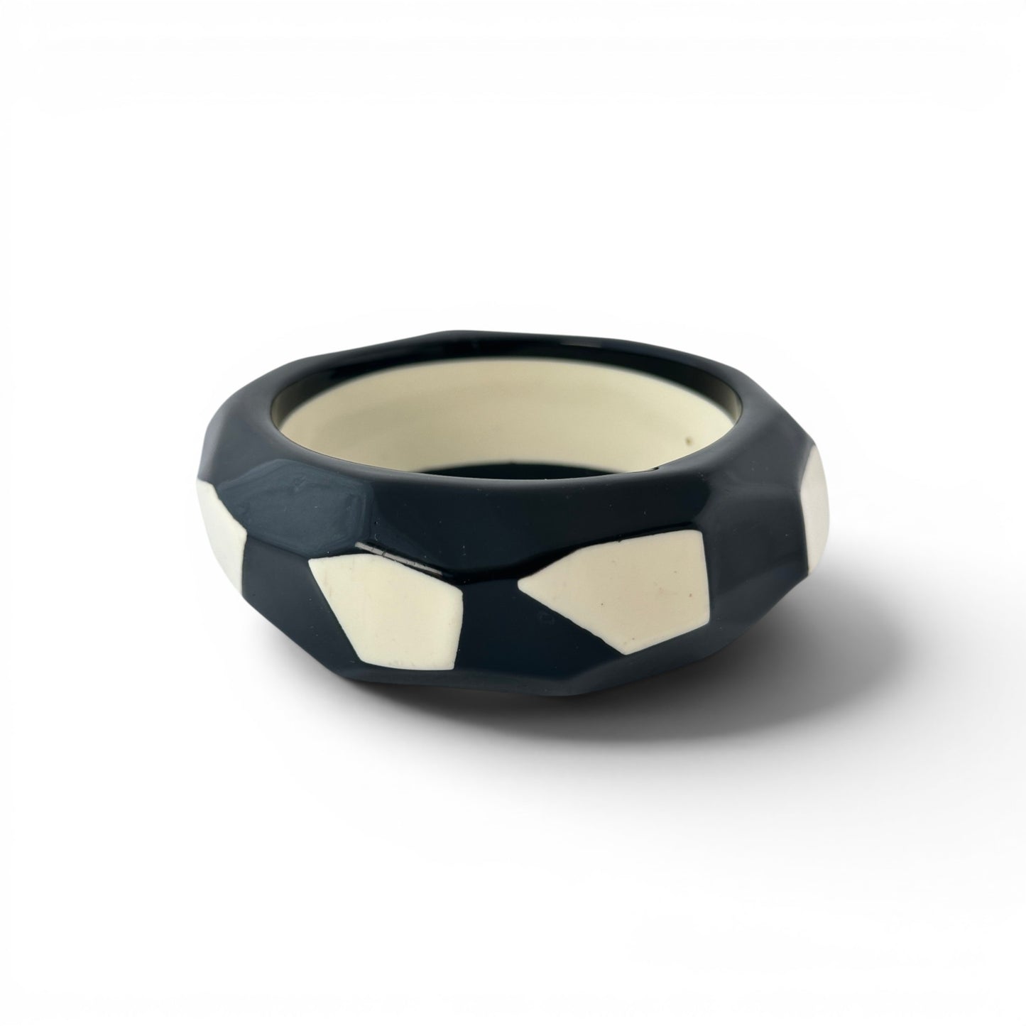 Wide black and cream Lucite bangle bracelet with faceted geometric exterior and flush cream polygonal inlay panels