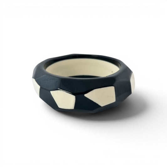 Wide black and cream Lucite bangle bracelet with faceted geometric exterior and flush cream polygonal inlay panels