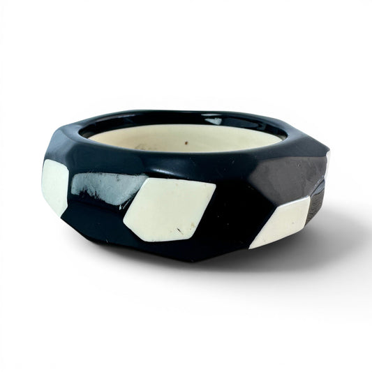 Top-down view of rigid black gloss bangle showing angular flat-cut facets and cream inlay panels distributed around outer ...