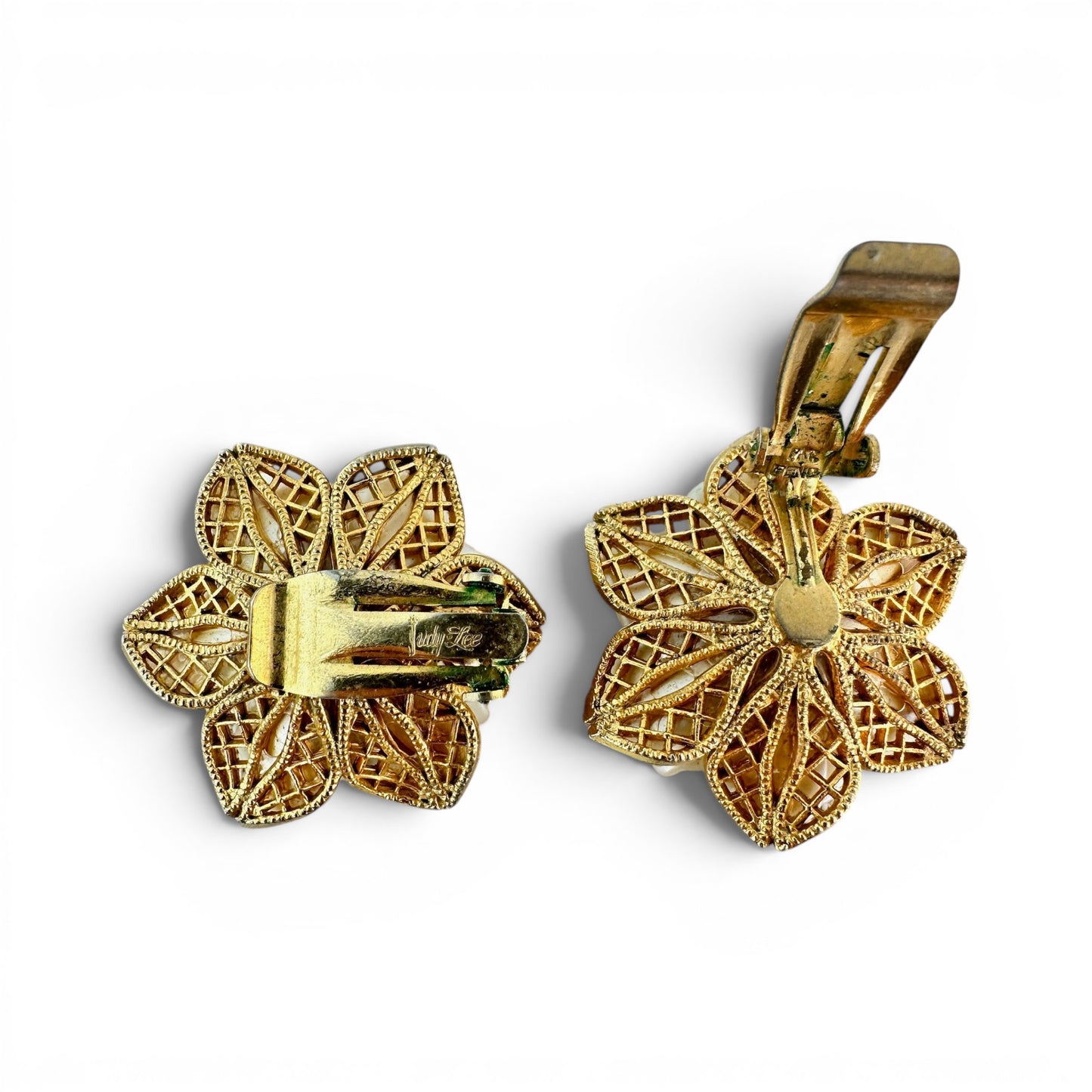 Rear view of gold-tone openwork flower-shaped clip settings showing cursive maker's signature stamp on hardware