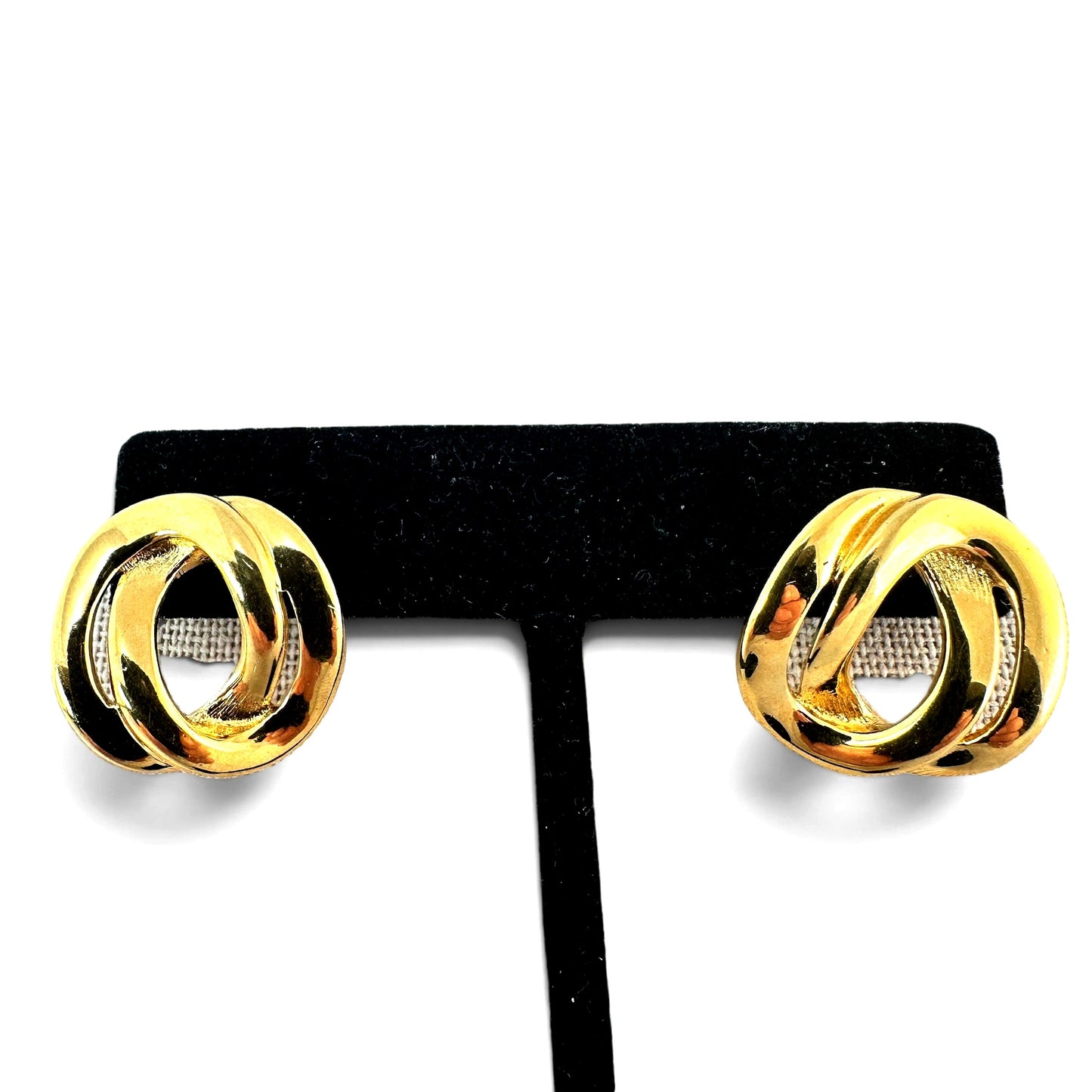 Gold-tone three-dimensional oval knot earrings displayed on black velvet T-bar stand, high-polish front face