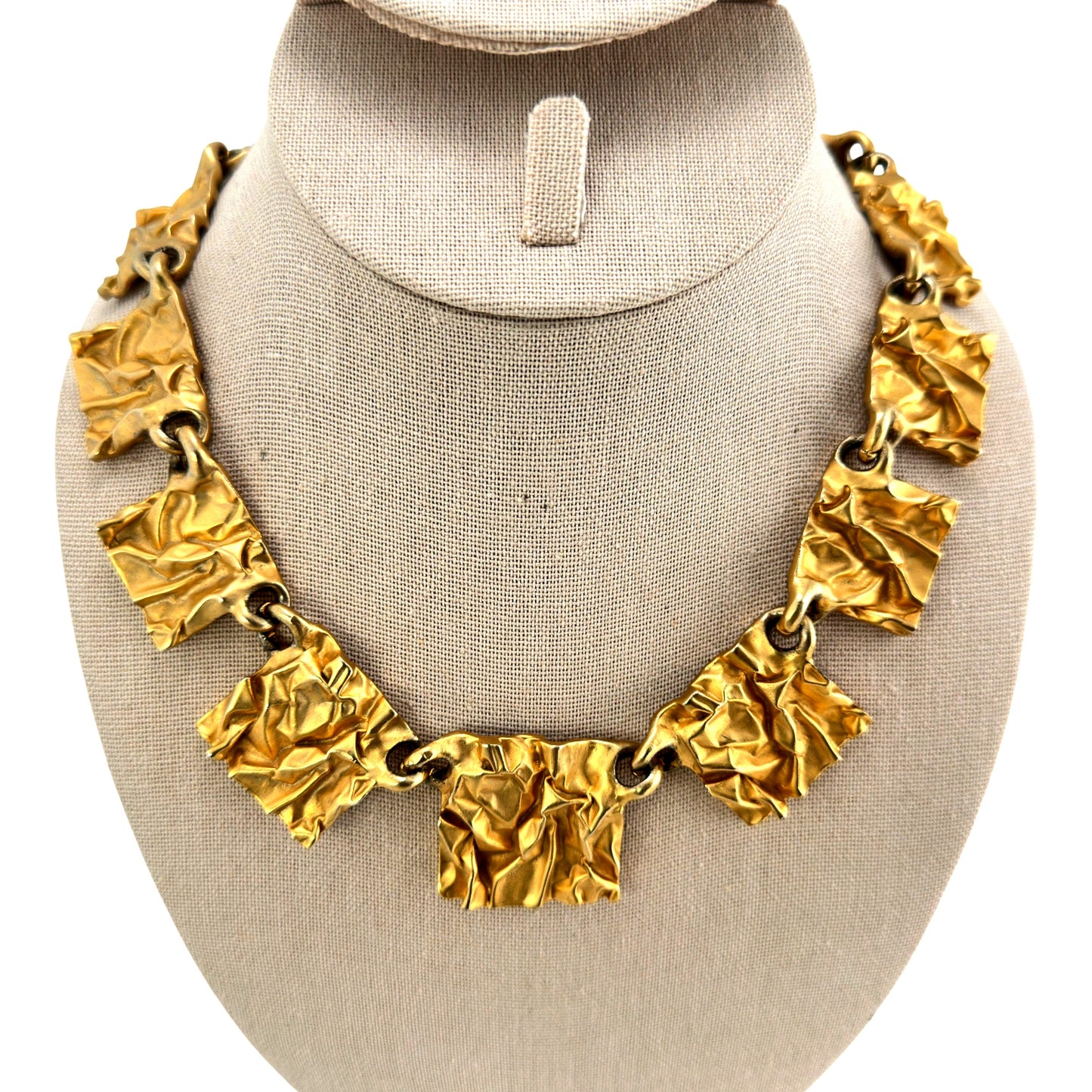 Gold-tone statement necklace with crumpled rectangular gilt plaques linked by large round jump rings, shown on linen bust