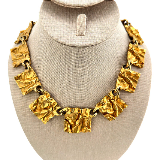 Gold-tone statement necklace with crumpled rectangular gilt plaques linked by large round jump rings, shown on linen bust