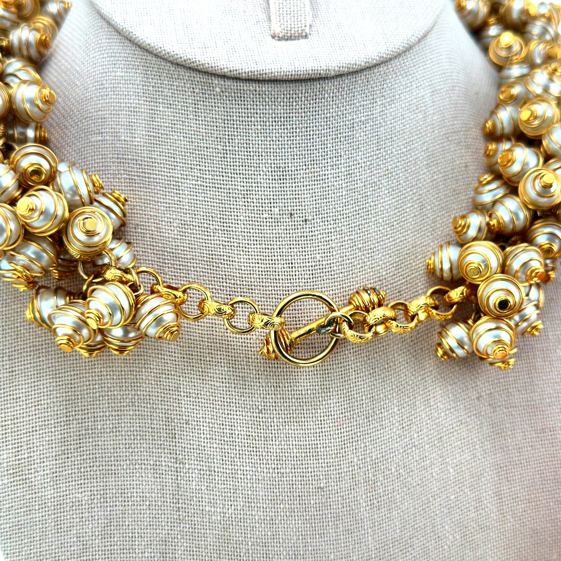 Close-up of spiral gold-tone wire-caged faux pearl beads and ornate ring-and-bar toggle clasp on bib necklace, back view