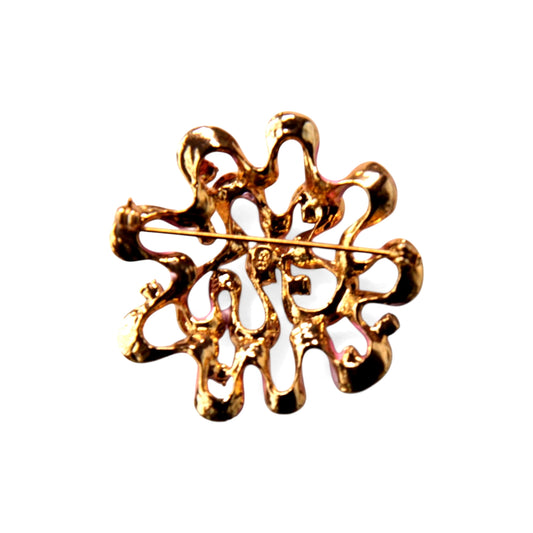 Reverse of circular gold-tone cast brooch showing rollover safety clasp, straight pin stem, and small stamped mark near ce...