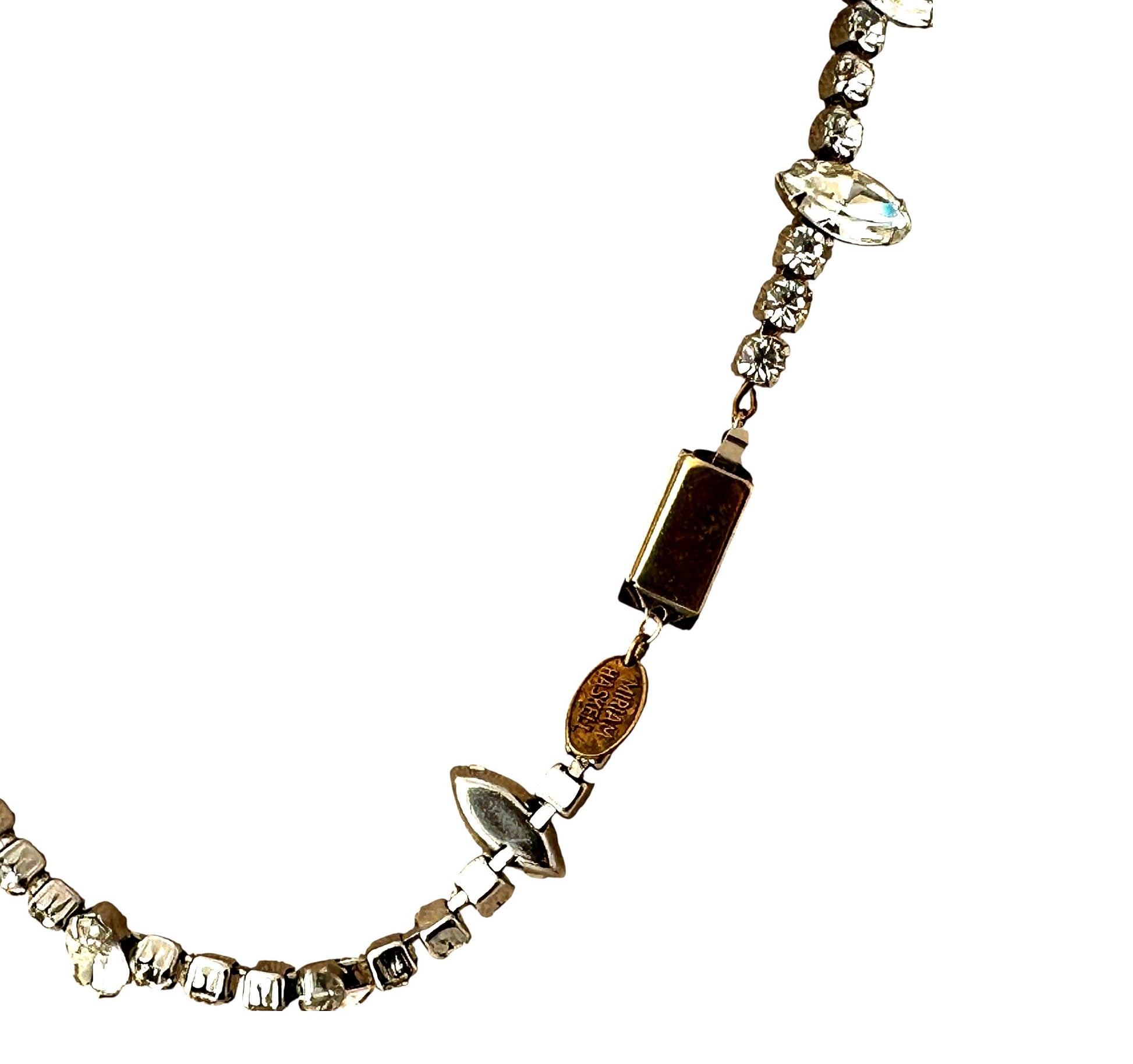 Close-up of oval Miriam Haskell hang tag stamped in lettering, attached to rectangular box clasp with aged gold-tone patina