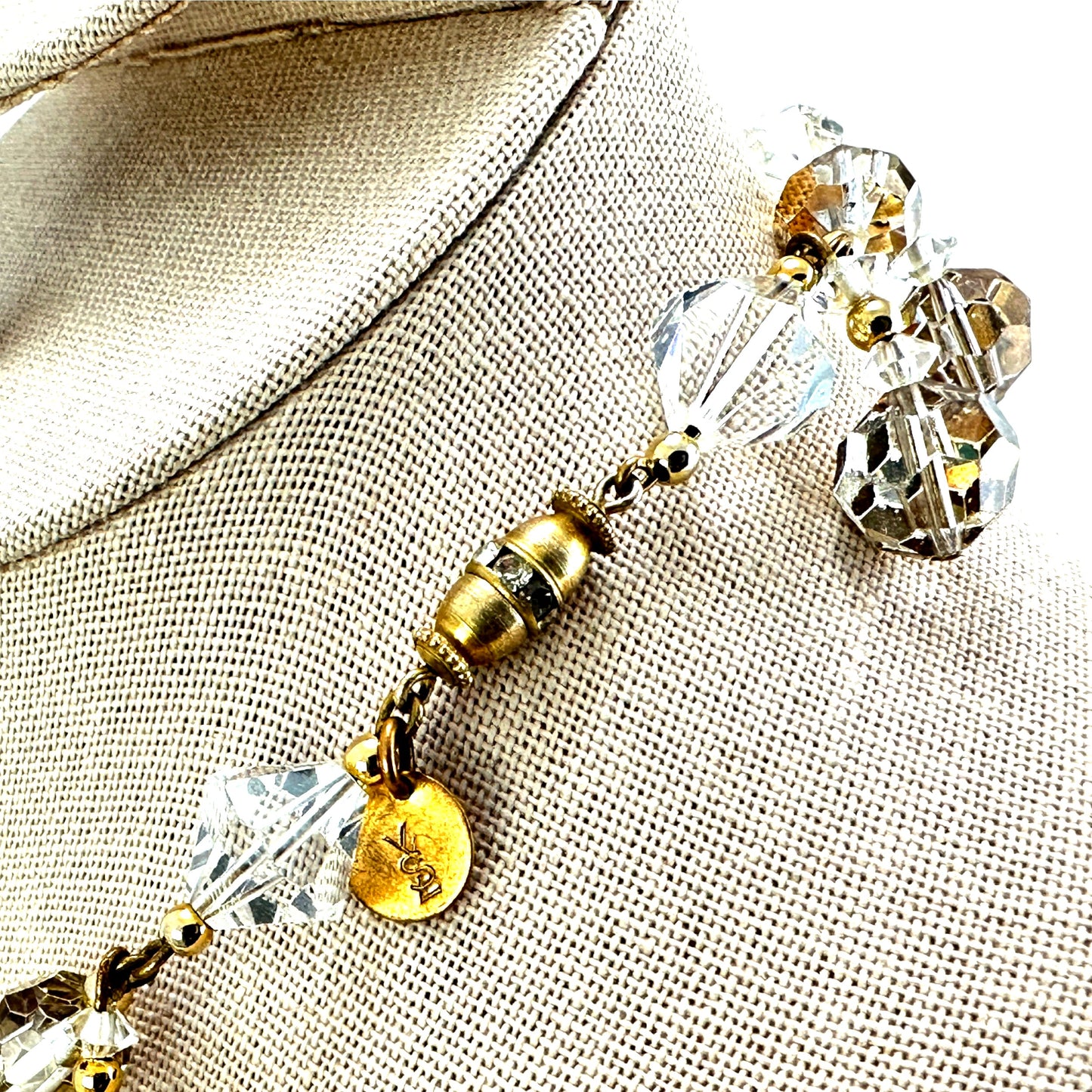 Close-up of gold-tone barrel clasp with rhinestone accent ring and small oval YSL stamped hang tag on jump ring