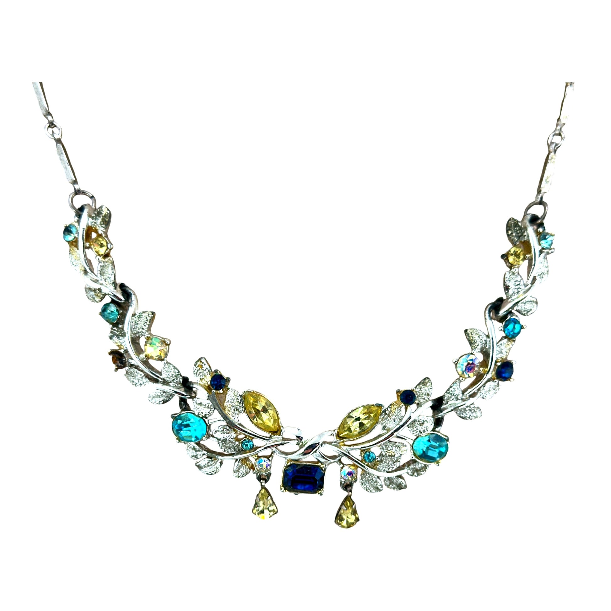 Close-up of Coro bib necklace centerpiece showing emerald-cut blue stone flanked by teal oval and yellow-green marquise rh...